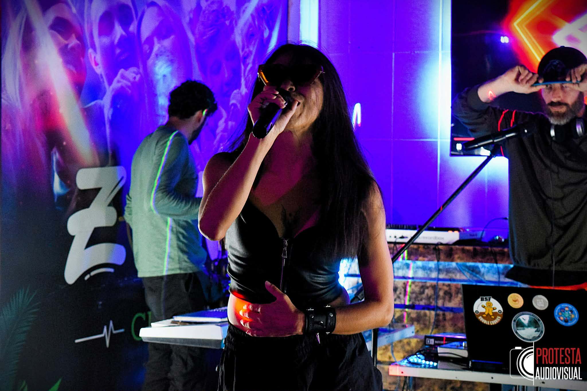 Andrea Vaca cantando con micrófono bajo luces de colores